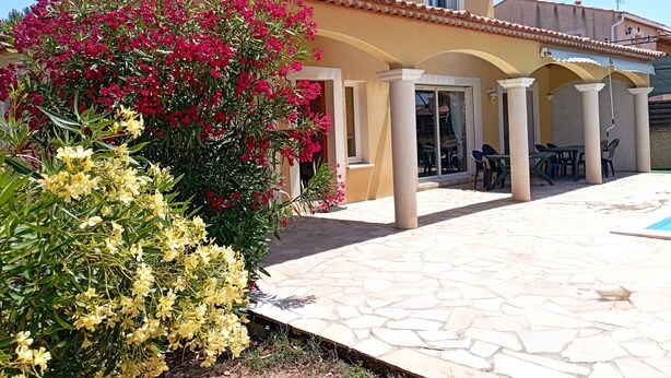 Una casa de dos pisos con techo de tejas, un porche cubierto con mobiliario exterior y una piscina.