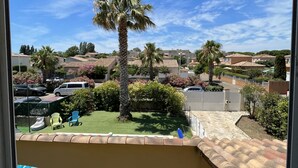 Vista desde un balcón con vista a una piscina, palmeras y una zona residencial con casas y coches aparcados.