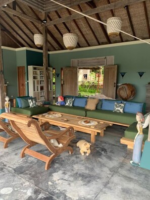 A cozy living room with a green sofa, wooden coffee table, and rocking chairs. A small dog is visible on the floor.