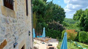An outdoor patio with stone walls, wooden tables, and blue umbrellas.