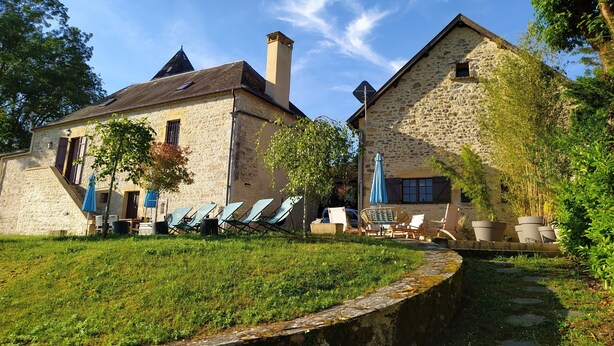 A stone building with a garden area featuring outdoor seating and umbrellas.