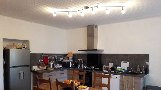 A compact kitchen with a refrigerator, stove, and microwave. There is a dining table with chairs and a bowl of fruit. - EXPOSED STONE HOUSE (Ancelle)
