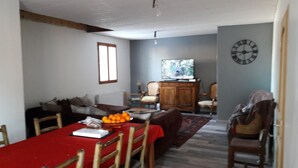 A dining area with a red table, wooden chairs, a wooden cabinet, and a television. - EXPOSED STONE HOUSE (Ancelle)