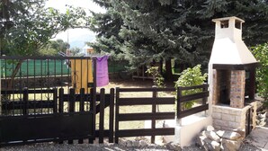 A rustic outdoor area with a brick-built structure, possibly a barbecue or oven, surrounded by a wooden fence and gravel ground. - EXPOSED STONE HOUSE (Ancelle)