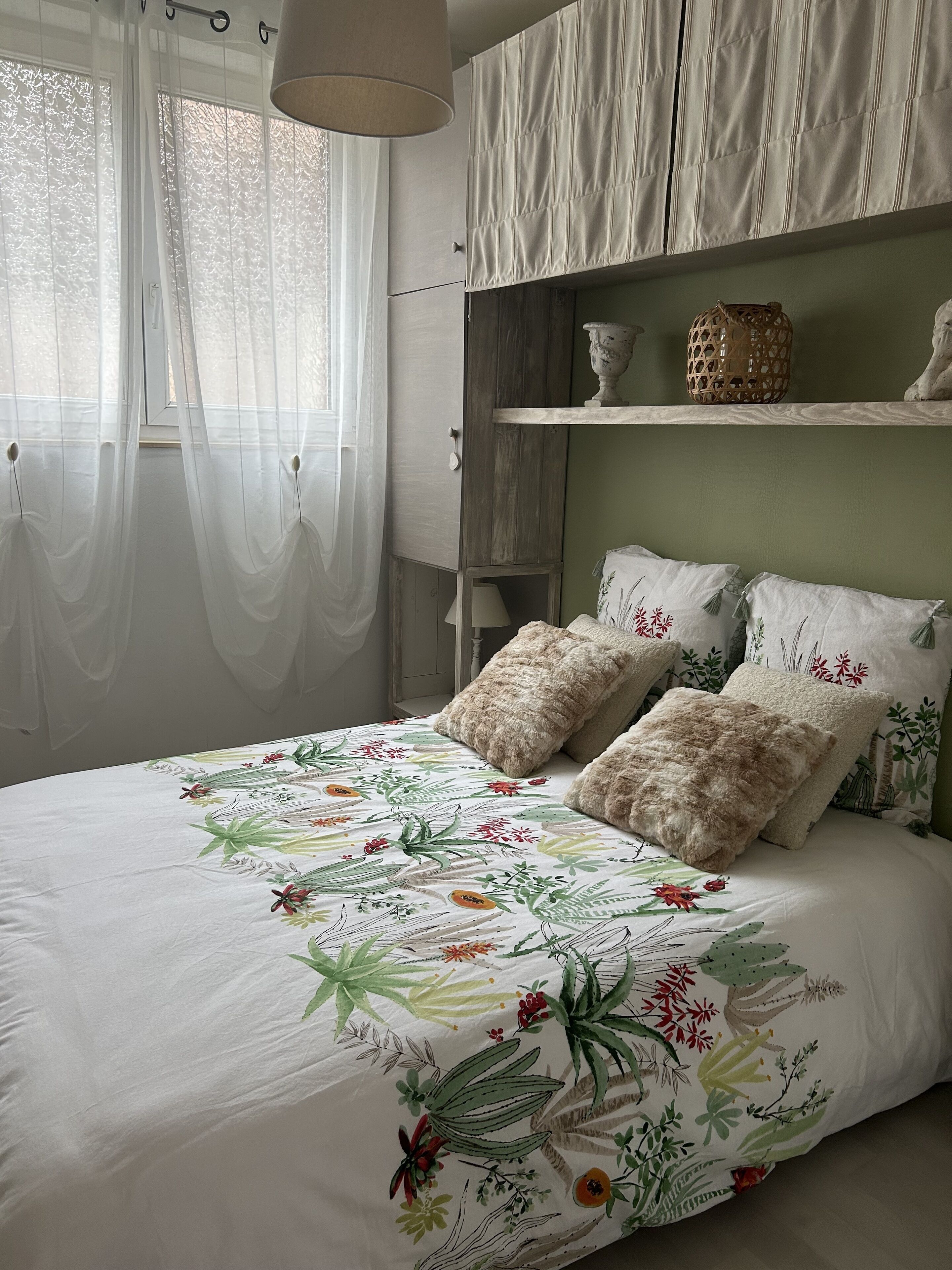 Ein Schlafzimmer mit blumigem Bettbezug, einem hölzernen Kopfteil und einem Nachttisch mit Lampe.