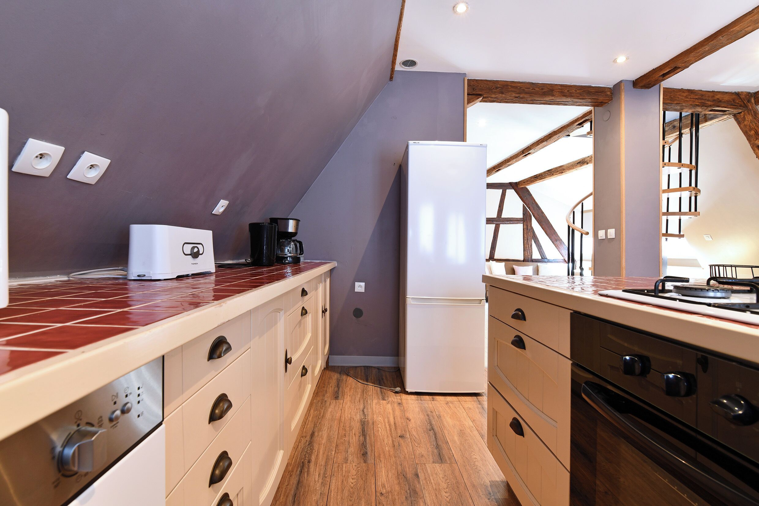 Una cocina moderna con suelo de madera, horno empotrado y refrigerador.