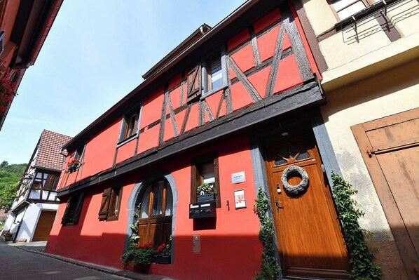 A traditional half-timbered building with a red facade, wooden door, and a visible mailbox. - Villa Joseph **, Apartment 4 people in Kaysersberg - 2 bedrooms (Kaysersberg-Vignoble)