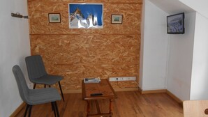 A room with a sloped ceiling, wooden wall paneling, a wooden table with a remote control, a gray chair, and two framed pictures on the wall. - 4-seater apartment 50 m2 (Laruns)