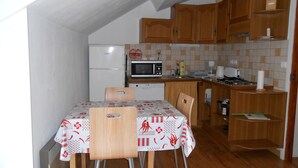 A small kitchen with wooden cabinets, a microwave, a refrigerator, and a dining table with chairs. - 4-seater apartment 50 m2 (Laruns)