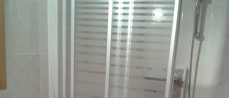 A bathroom with a glass shower enclosure, a white sink, and a blue soap dispenser.