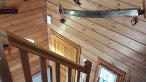 A wooden staircase with a handrail, a window with a curtain, and a saw blade mounted on the wall.