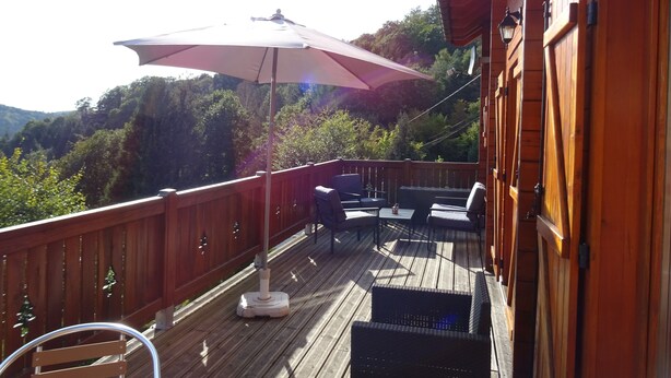A wooden deck with outdoor furniture, including chairs and a table, and a large umbrella providing shade.