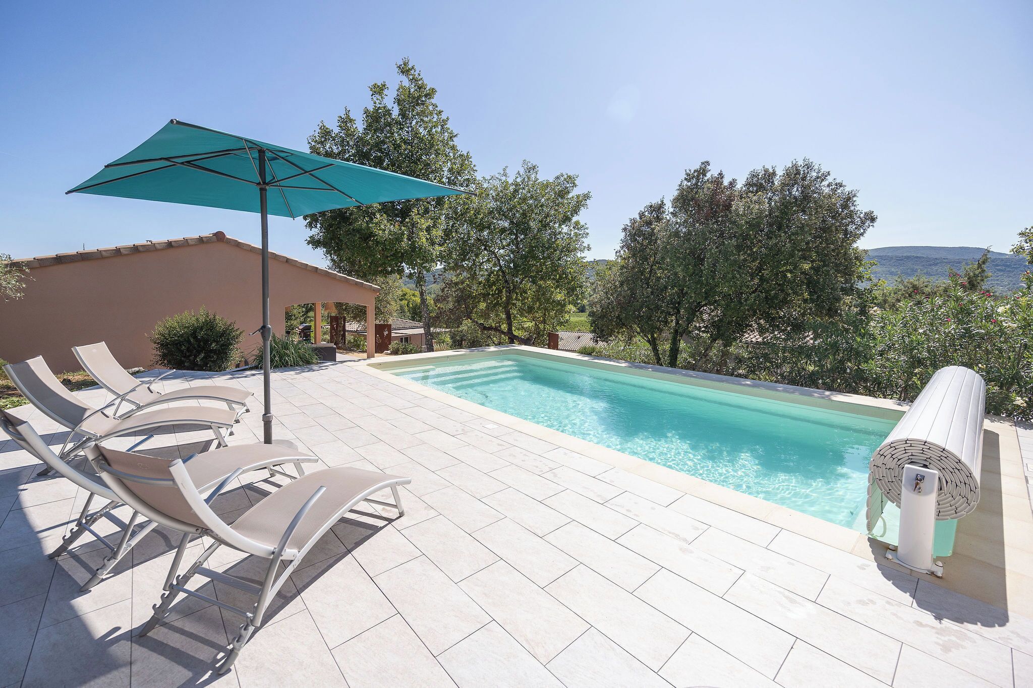 Una piscina con lettini e un ombrellone, circondata da alberi e con vista sul mare.