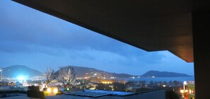 Vista desde la azotea de un paisaje urbano al anochecer, con edificios iluminados y una masa de agua en la distancia.
