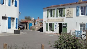 Una calle estrecha flanqueada por edificios, incluyendo una construcción blanca con contraventanas verdes y un letrero que dice 'Tantine Berthe'.