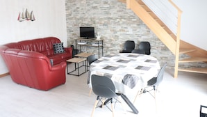 Una sala de estar con un sofá de cuero rojo, una mesa de comedor con sillas, un televisor sobre un mueble bajo y una escalera.