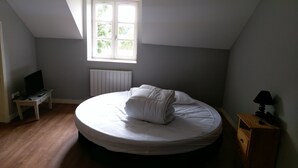 Een slaapkamer met een enkel bed, een klein nachtkastje met een televisie en afstandsbediening, een raam met uitzicht op groen, en een radiator.