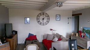 Een woonkamer met een grote wandklok, een televisie en een bank met rode kussens.