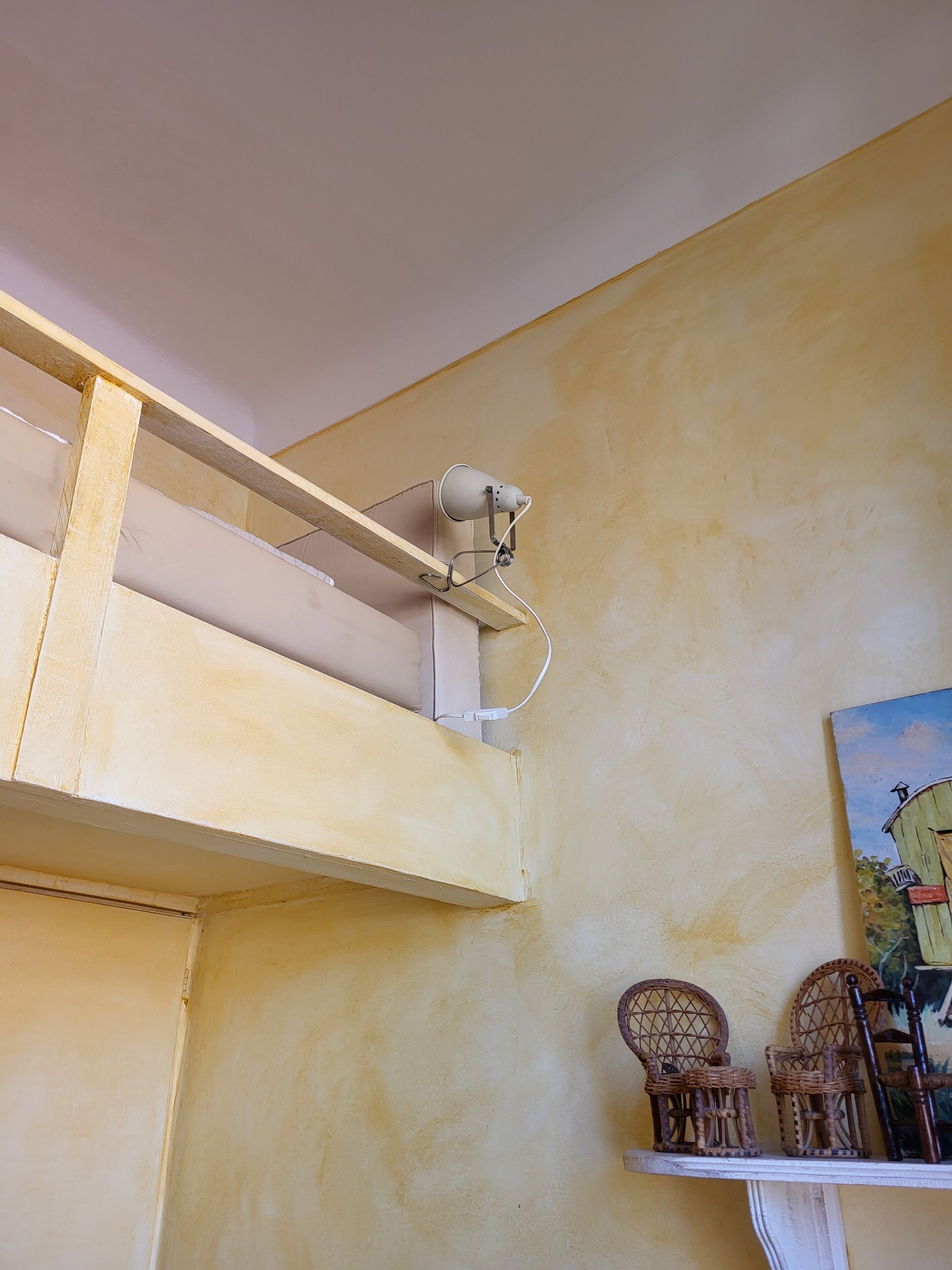 A room with a high ceiling, a white ceiling fan, and a painting of a house on the wall.