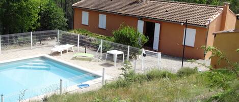 Una casa con piscina, rodeada por una cerca blanca, y vista a un área boscosa.
