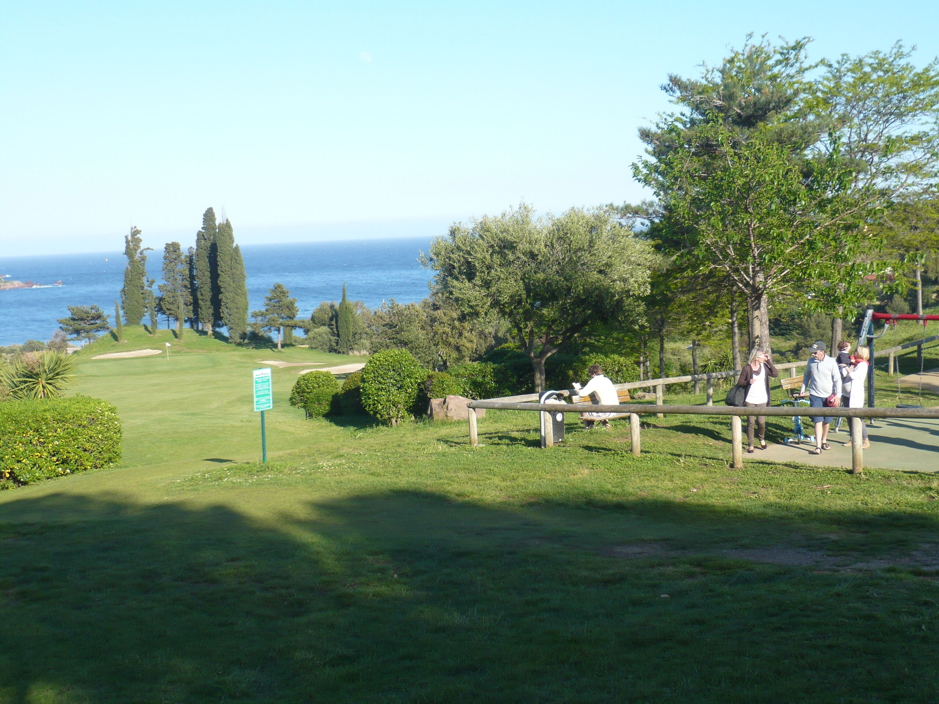 En golfbana med utsikt över havet, en träbänk och en vägskylt.