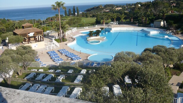 Een resort zwembad met meerdere ligbedden en uitzicht op zee.