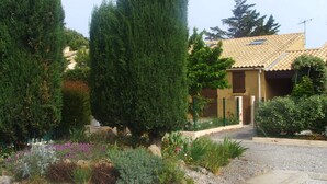 Una casa con tetto in tegole, circondata da un vialetto sterrato e diverse piante.