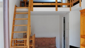 Una stanza con un letto a castello, una scala in legno, un divano, una televisione su un mobile in legno e un armadio.
