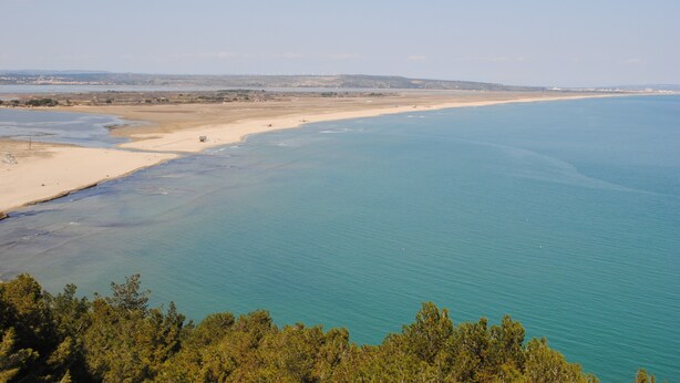 Paesaggio costiero con spiaggia sabbiosa, acque cristalline e una linea di costa in lontananza.