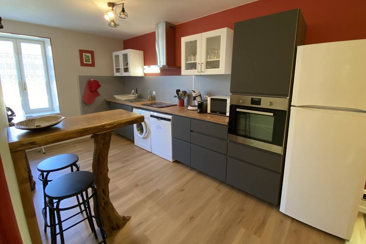 A modern kitchen with a wooden table, bar stools, a washing machine, a microwave, and a refrigerator.