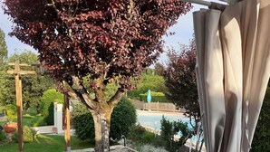 Un espace aménagé au bord de la piscine, avec une pergola, un arbre aux feuilles rouges et un coin salon abrité.