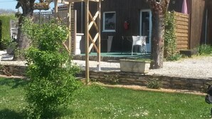 Une maison avec une pergola, une terrasse avec une table et des chaises, et un jardin agrémenté de fleurs blanches.