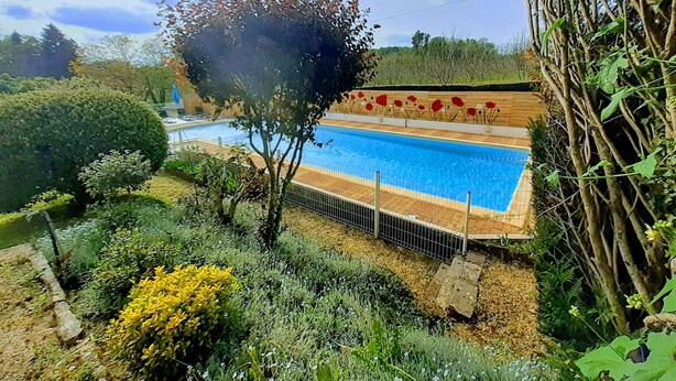 Une piscine entourée d’une végétation luxuriante et une terrasse en bois agrémentée de décorations florales rouges.