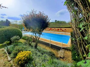 A swimming pool surrounded by lush greenery and a wooden deck with red flower decorations.