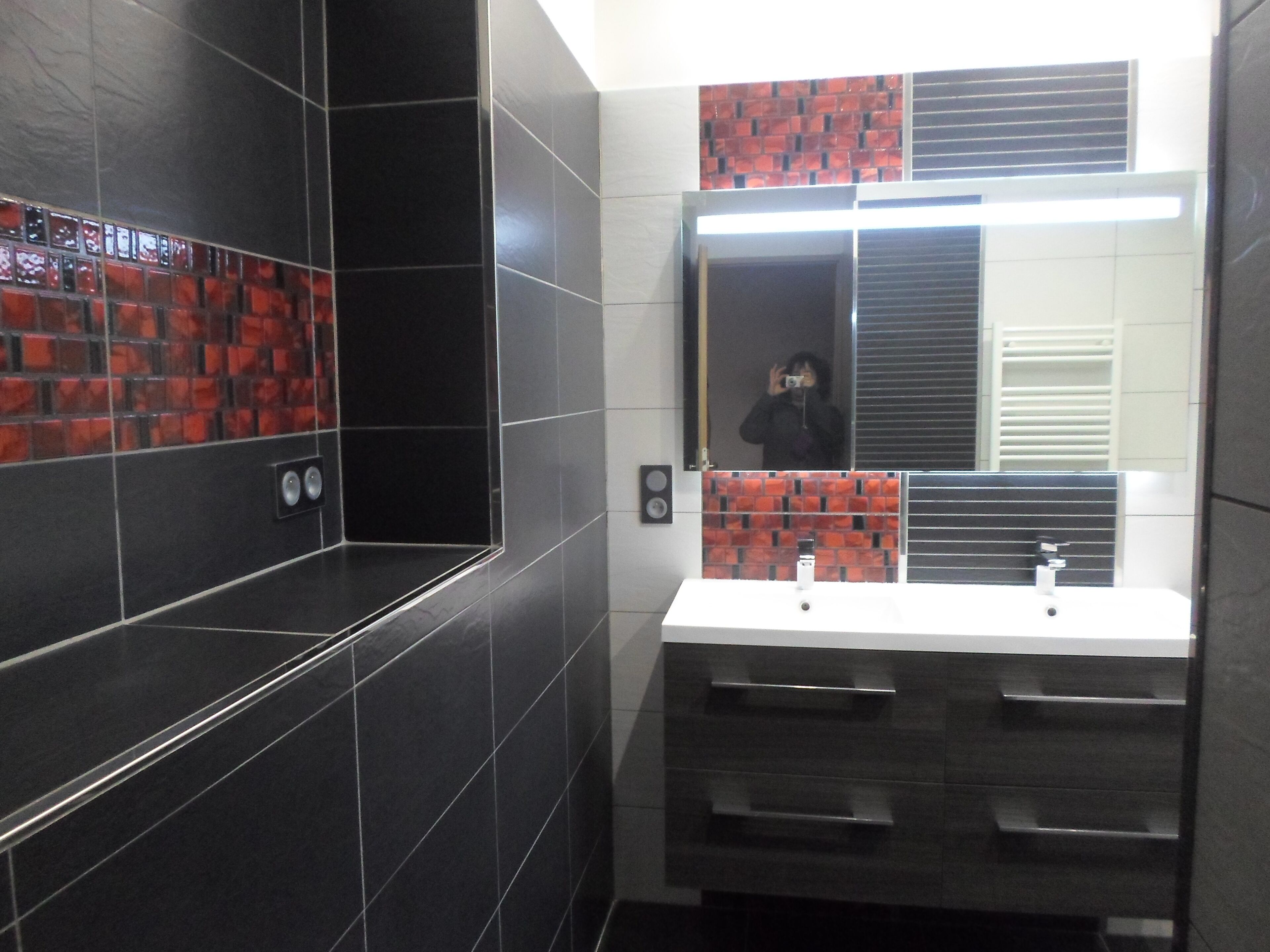 Un bagno moderno con pareti piastrellate in nero e rosso, uno specchio grande e un lavandino bianco.