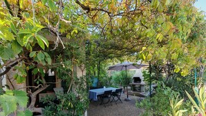 A garden patio with a table and chairs, surrounded by various plants and a stone structure. - Rental Porticcio Agosta Air conditioning 200 m from the sea, garden and barbecue (Albitreccia)