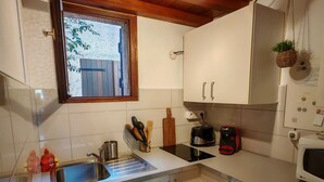 A compact kitchen with white cabinets, a built-in dishwasher, a microwave, and a window with a view of the outside. - Rental Porticcio Agosta Air conditioning 200 m from the sea, garden and barbecue (Albitreccia)