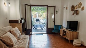 A cozy living room with a sofa, a TV, and a view of the outside patio area. - Rental Porticcio Agosta Air conditioning 200 m from the sea, garden and barbecue (Albitreccia)
