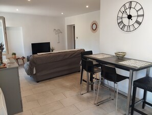 A modern living room with a sofa, a dining table with chairs, a TV, and a decorative wall clock.