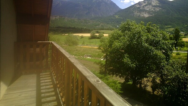 Un balcon donnant sur un paysage de montagnes, un arbre et un champ verdoyant.