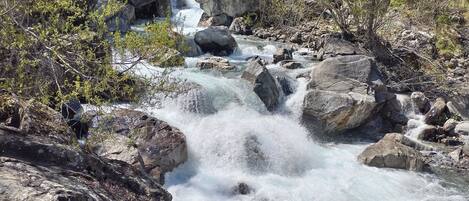 Une rivière aux eaux claires qui serpente entre les rochers, bordée d’arbres et dominée par un paysage montagneux.