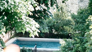 Une piscine entourée d’une végétation luxuriante, de murs en pierre et d’un bâtiment en pierre en arrière-plan.