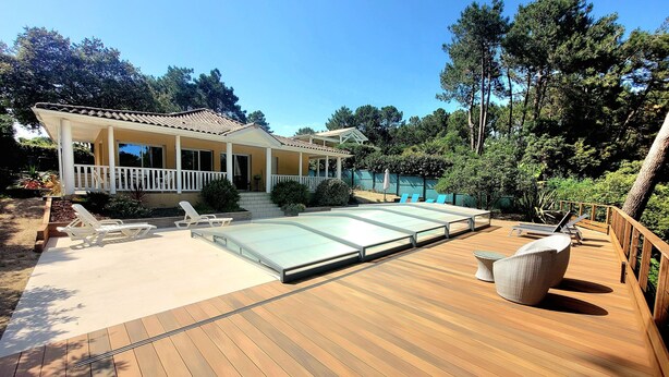 En træterrasse med swimmingpool, liggestole og et hus med veranda.