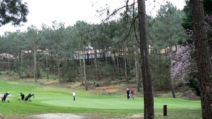 En golfbane med sandbunker, træer og en bygning i baggrunden.