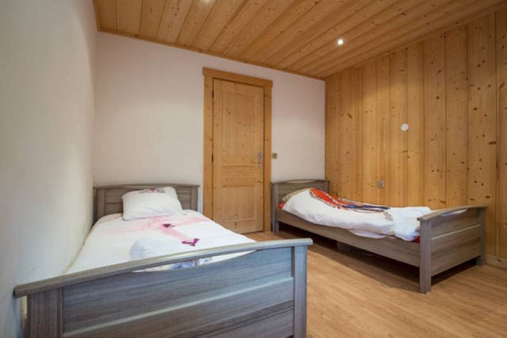 A bedroom with two wooden beds, a wooden wardrobe, and a wooden ceiling.