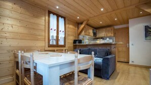 L’intérieur d’un chalet accueillant, avec une table à manger en bois, des chaises, un canapé et un coin cuisine.