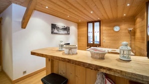 L’intérieur d’un chalet en bois comprend un coin cuisine avec un plan de travail en bois, un évier et une fenêtre avec des rideaux.