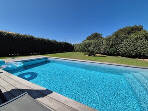 A rectangular swimming pool with clear blue water, surrounded by a wooden deck and a well-maintained hedge.