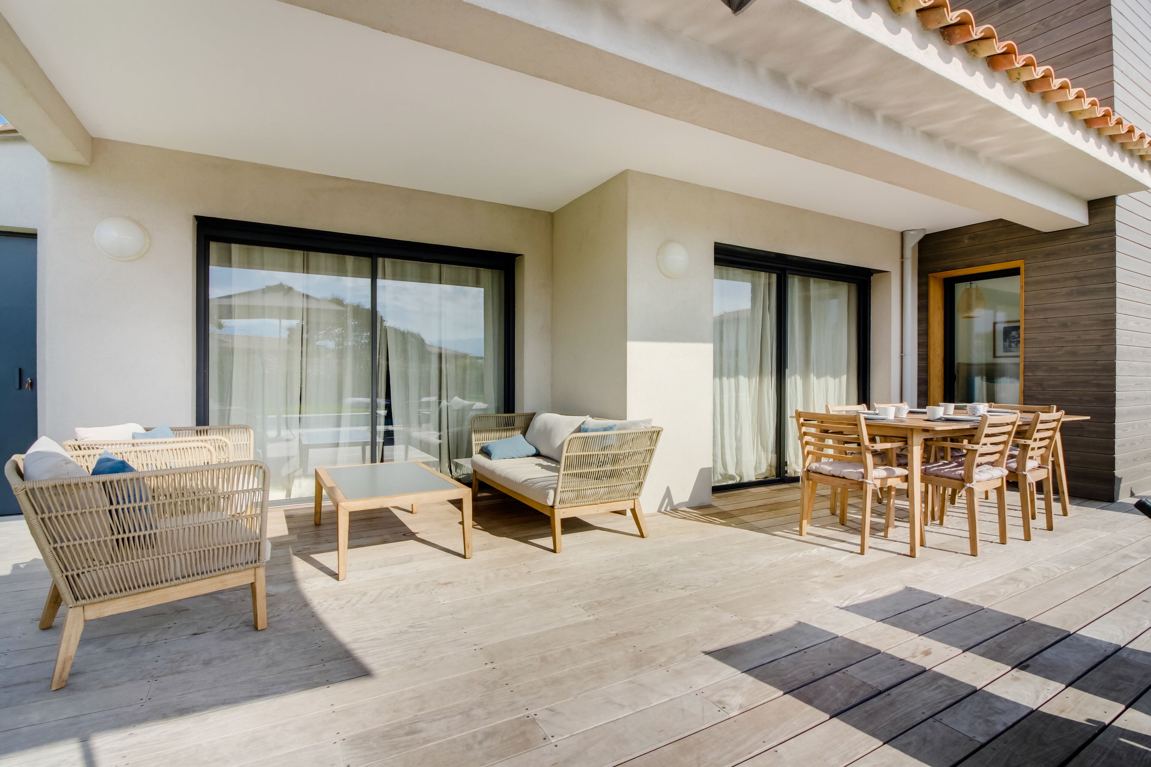 A modern outdoor patio with wicker furniture, a glass door, and a wooden table.