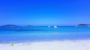 Ein Strand mit klarem, blauem Wasser, einem sandigen Ufer und ein paar Booten in der Ferne.